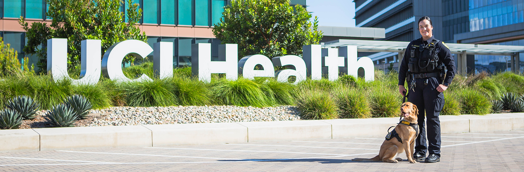 Officer Kolschefski standing with K-9 Amber in front of UCI Health sign
